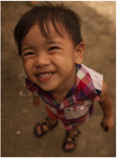A young boy from a country in Asia who is looking up at the camera from below and smiling